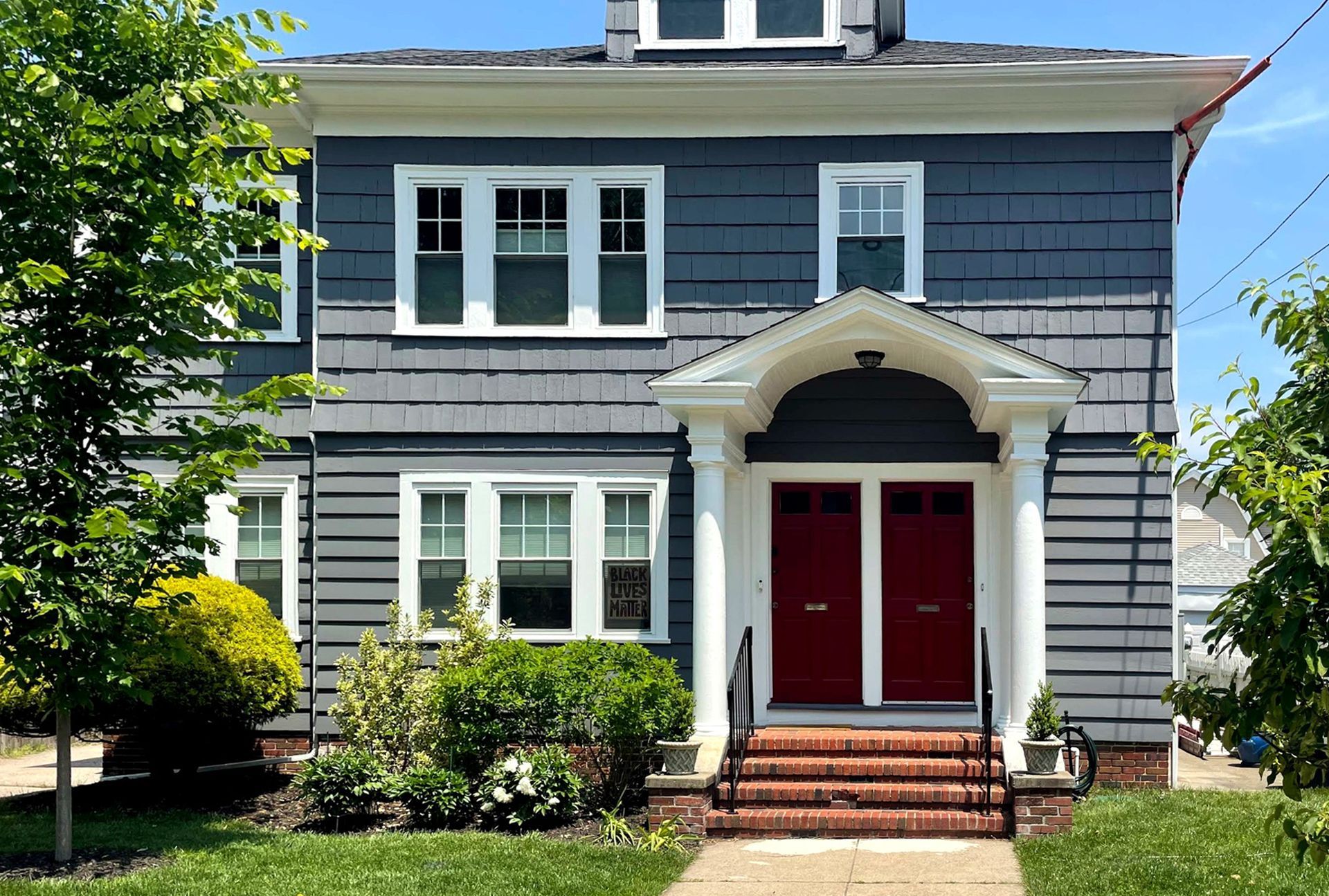 Gray two-story house with white trim, red front doors, and a small front lawn.
