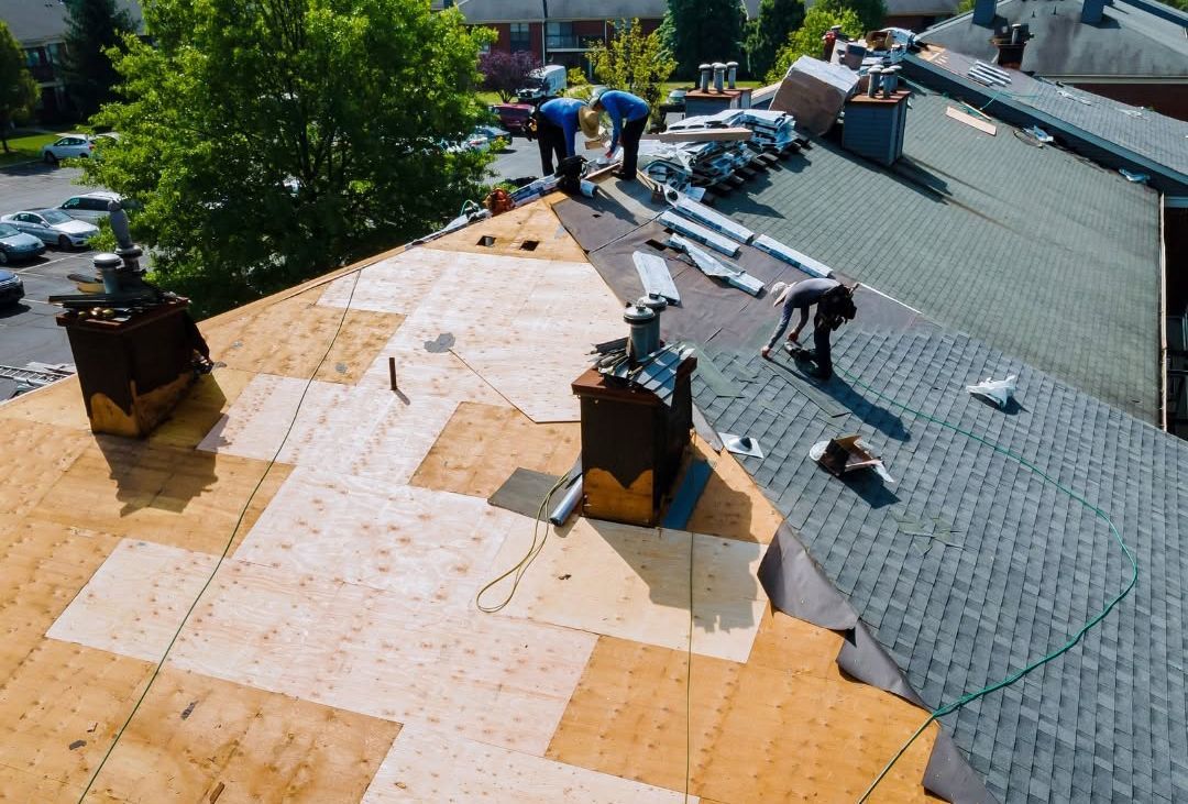 Roofers installing new shingles on a house roof, with one section partially completed and tools nearby.