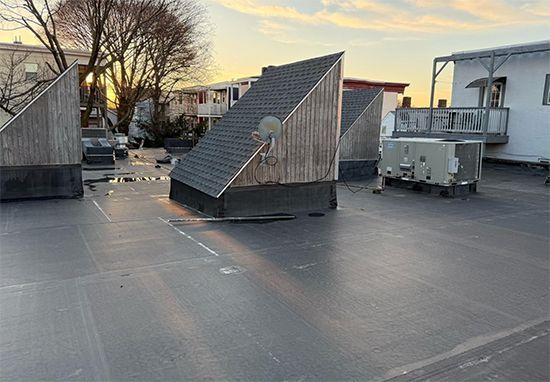 Flat rooftop with solar panels, HVAC units, and a sunset sky in the background