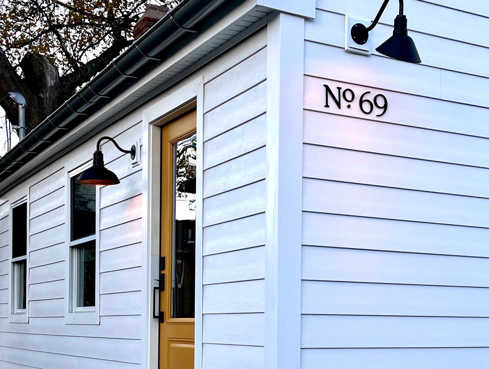 White building exterior with black lanterns and yellow door, marked “No. 69”