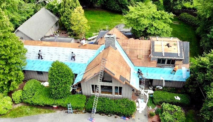 Aerial view of a large house with a blue roof, surrounded by trees and greenery.