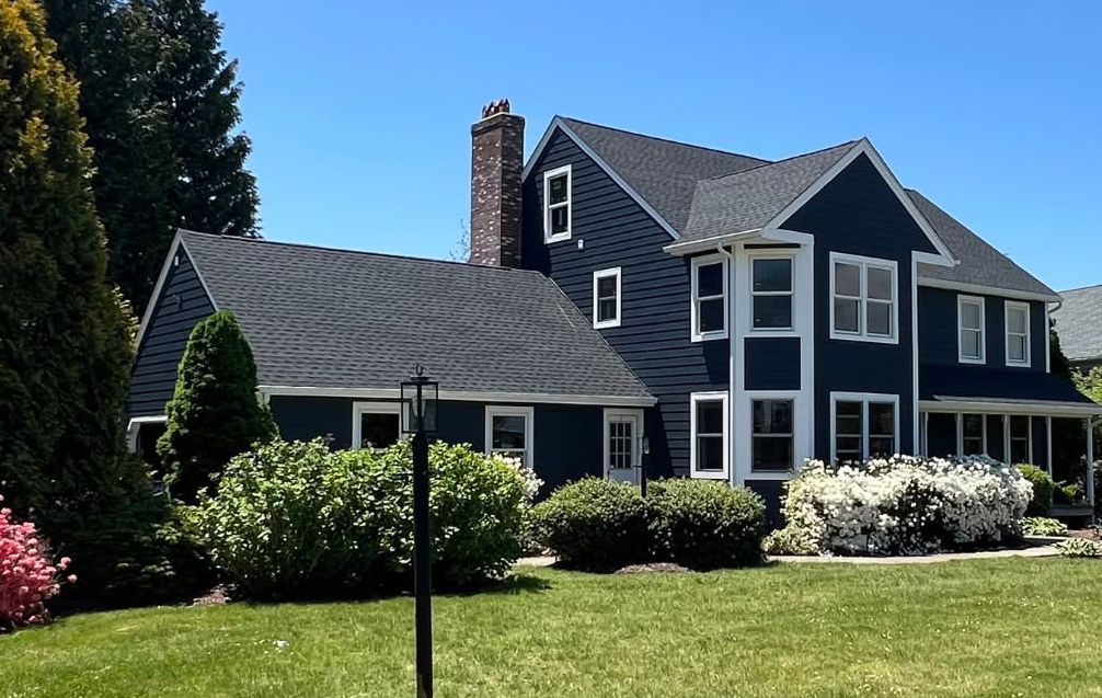 Large navy-blue house with white trim, manicured shrubs, and a green lawn under a clear blue sky