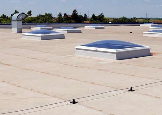 Rooftop with multiple white skylights on a flat beige surface under a clear sky.