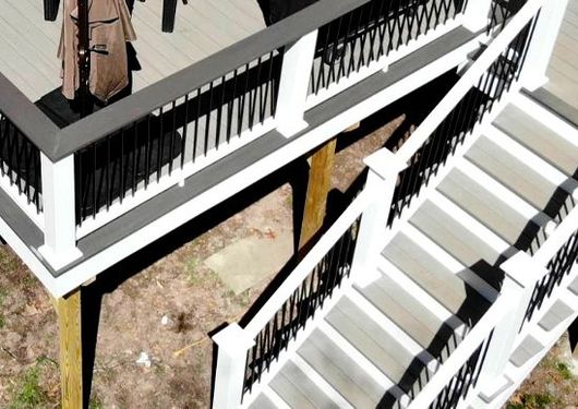 White staircase with black railings beside a raised wooden deck outdoors