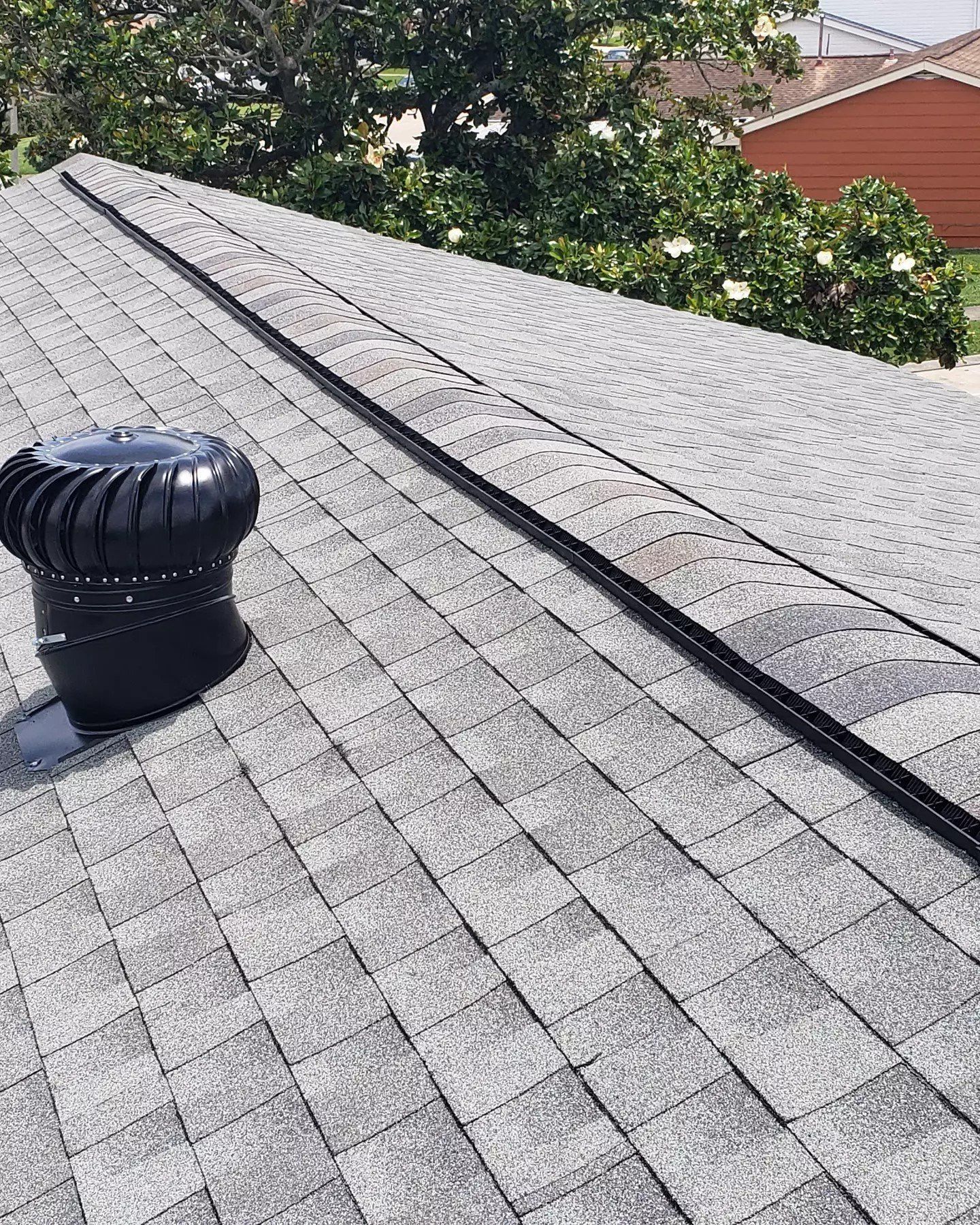 Gray shingled rooftop with a black vent pipe and trees in the background