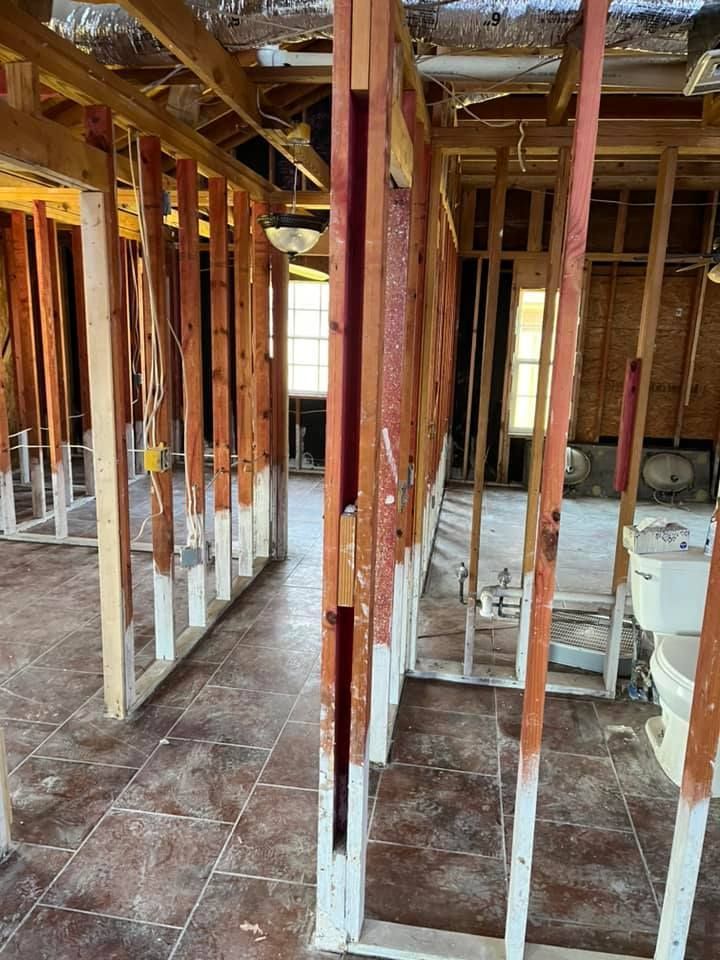 Interior of a gutted building under renovation, with exposed wooden studs and partially tiled floor.