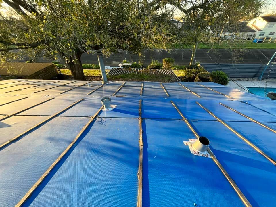 Blue tarp-covered roof with solar panels and a skylight in a tree-lined backyard