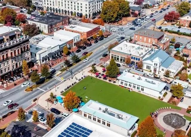 Aerial view of a town square with a green lawn, surrounding buildings, streets, and parked cars