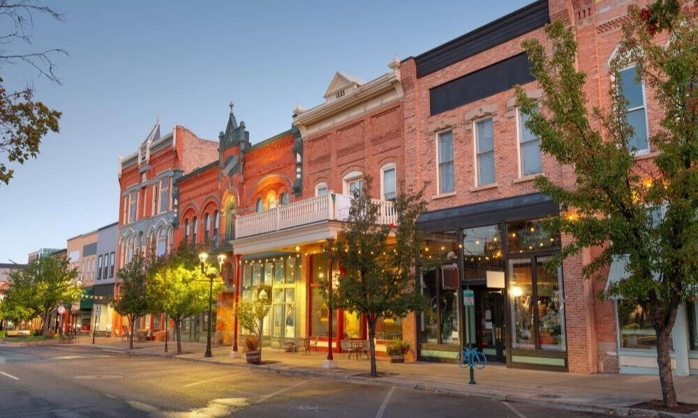 Historic downtown street with brick storefronts, glowing lights, and a few trees at dusk