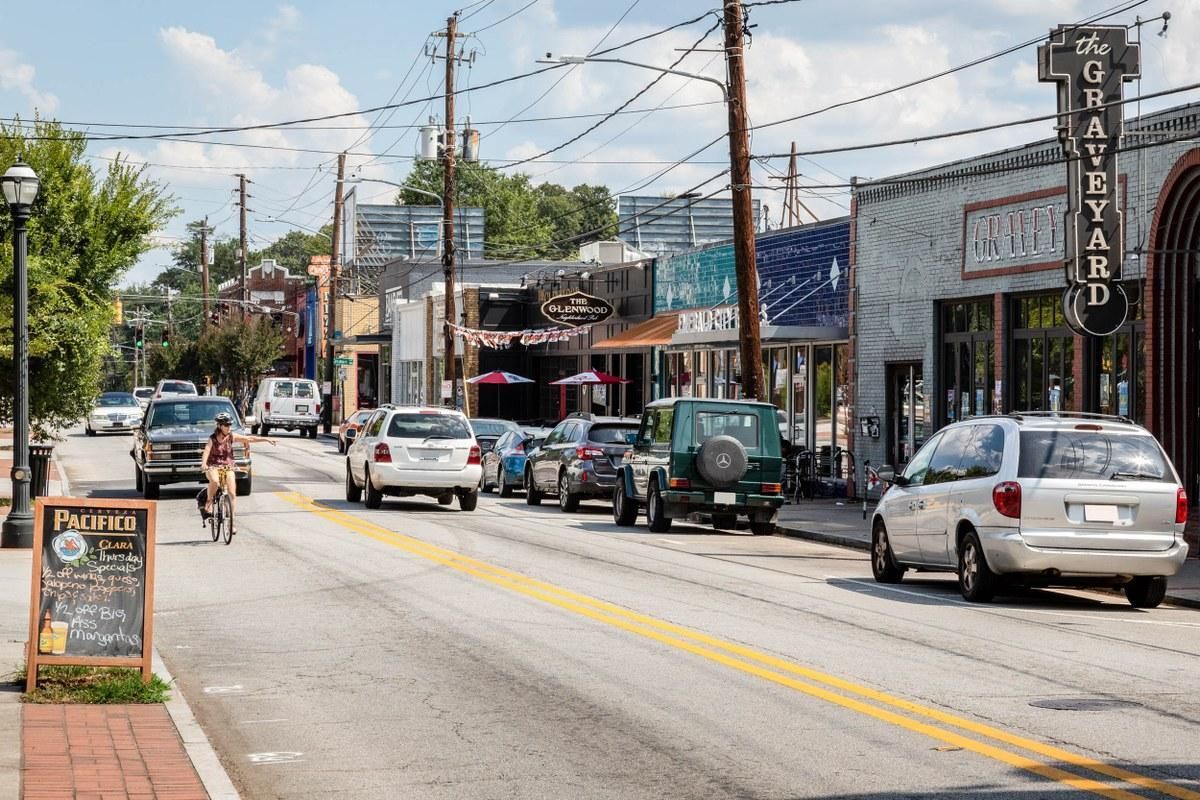 Busy small-town street with cars, a cyclist, and storefronts on a sunny day