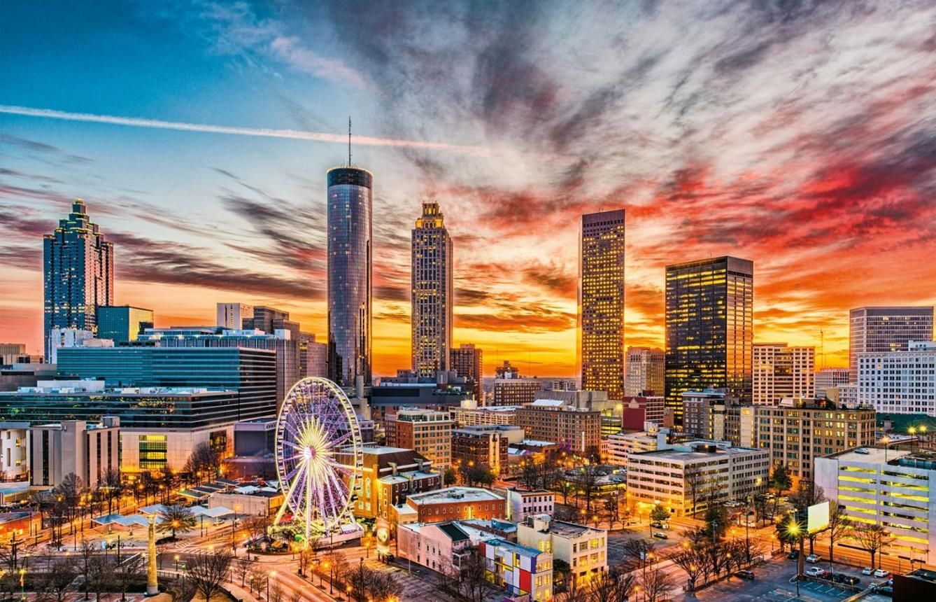 City skyline at sunset with a lit ferris wheel and dramatic orange-red clouds