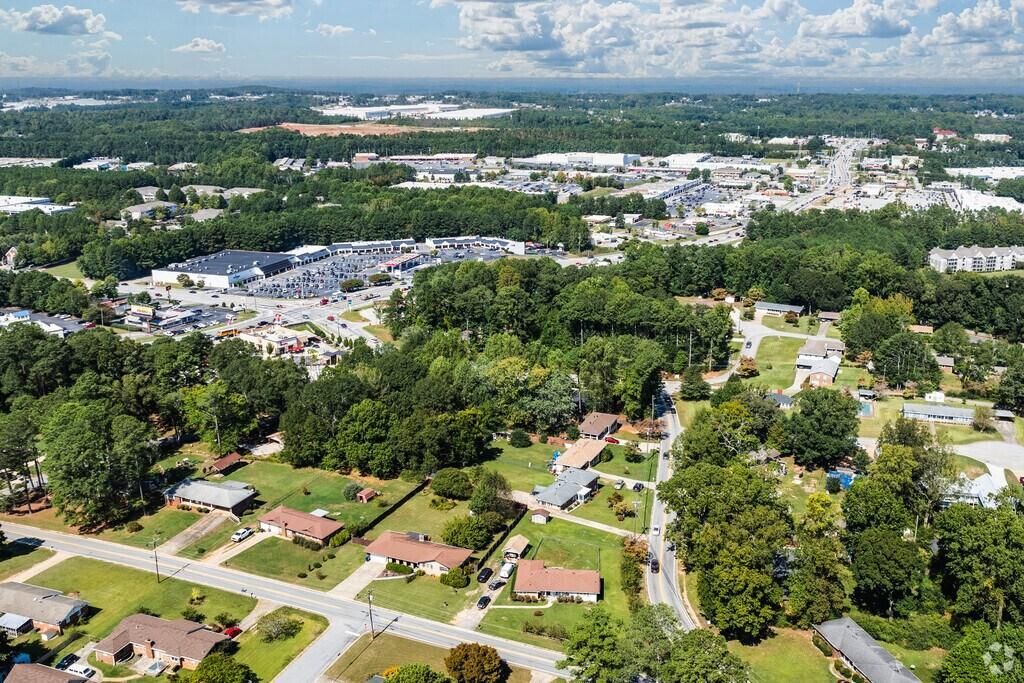 Aerial view of a suburban neighborhood with houses, roads, trees, and a distant city skyline under a cloudy sky