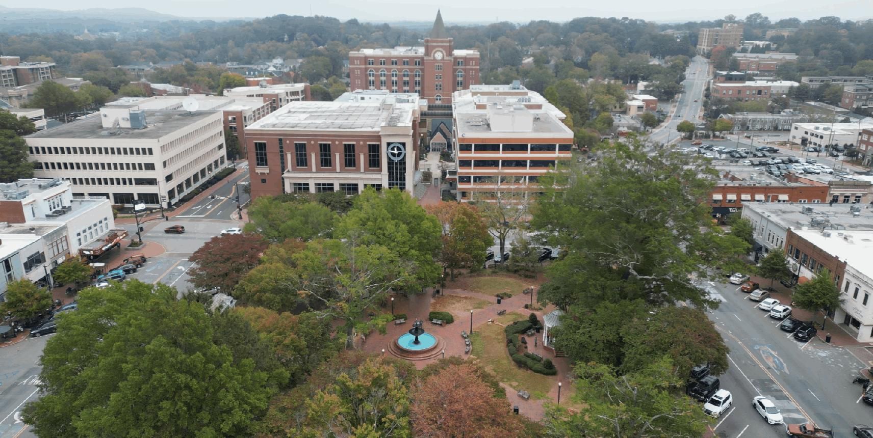 Aerial view of a town square with trees, roads, and surrounding buildings on an overcast day