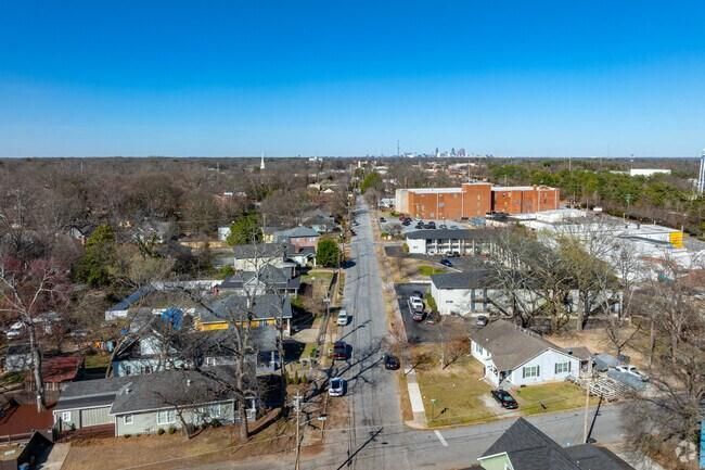 Aerial view of a neighborhood street with houses, trees, and a large brick building under a clear blue sky