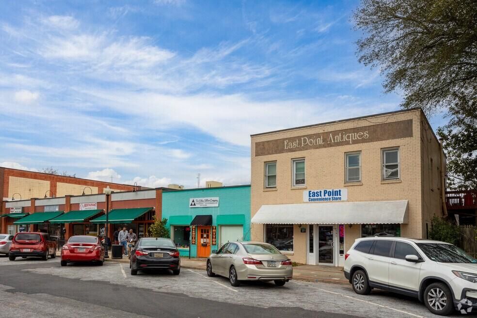 Small shopping strip with parked cars under a blue sky, including a tea shop and boutique storefronts.