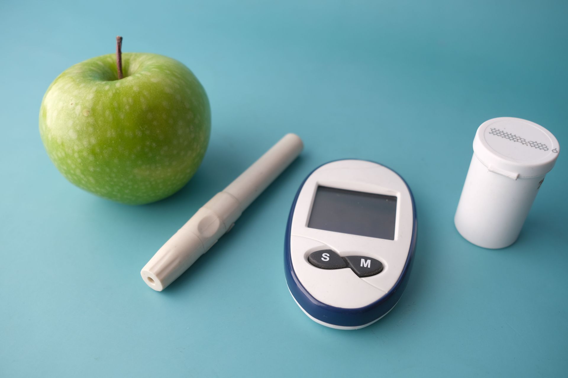 Green apple, glucose meter, and white insulin pen on a blue background