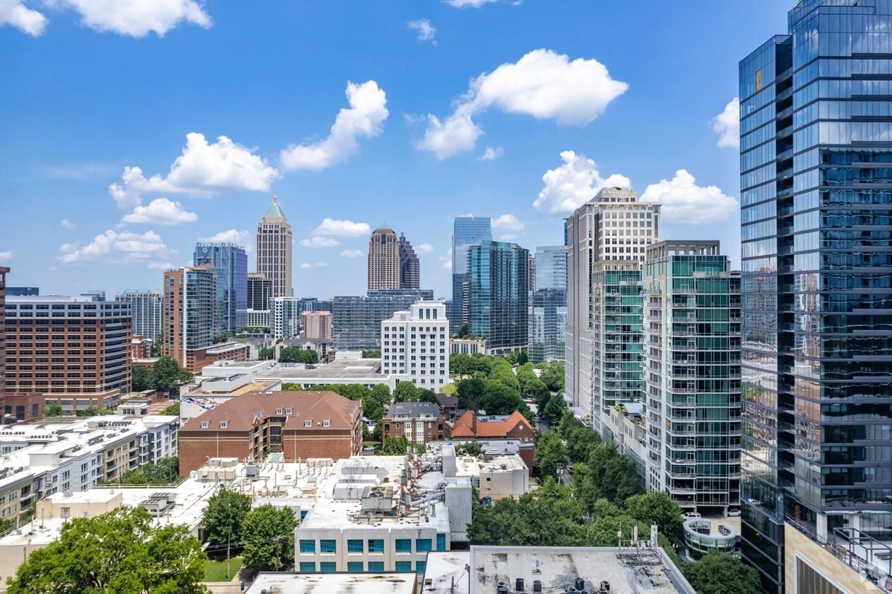 City skyline with modern high-rise buildings under a bright blue sky with scattered clouds.
