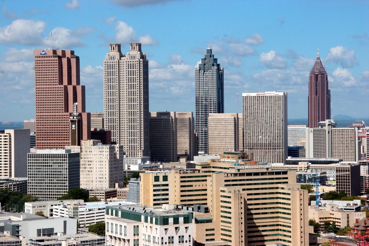 City skyline with tall downtown buildings under a bright blue sky and scattered clouds