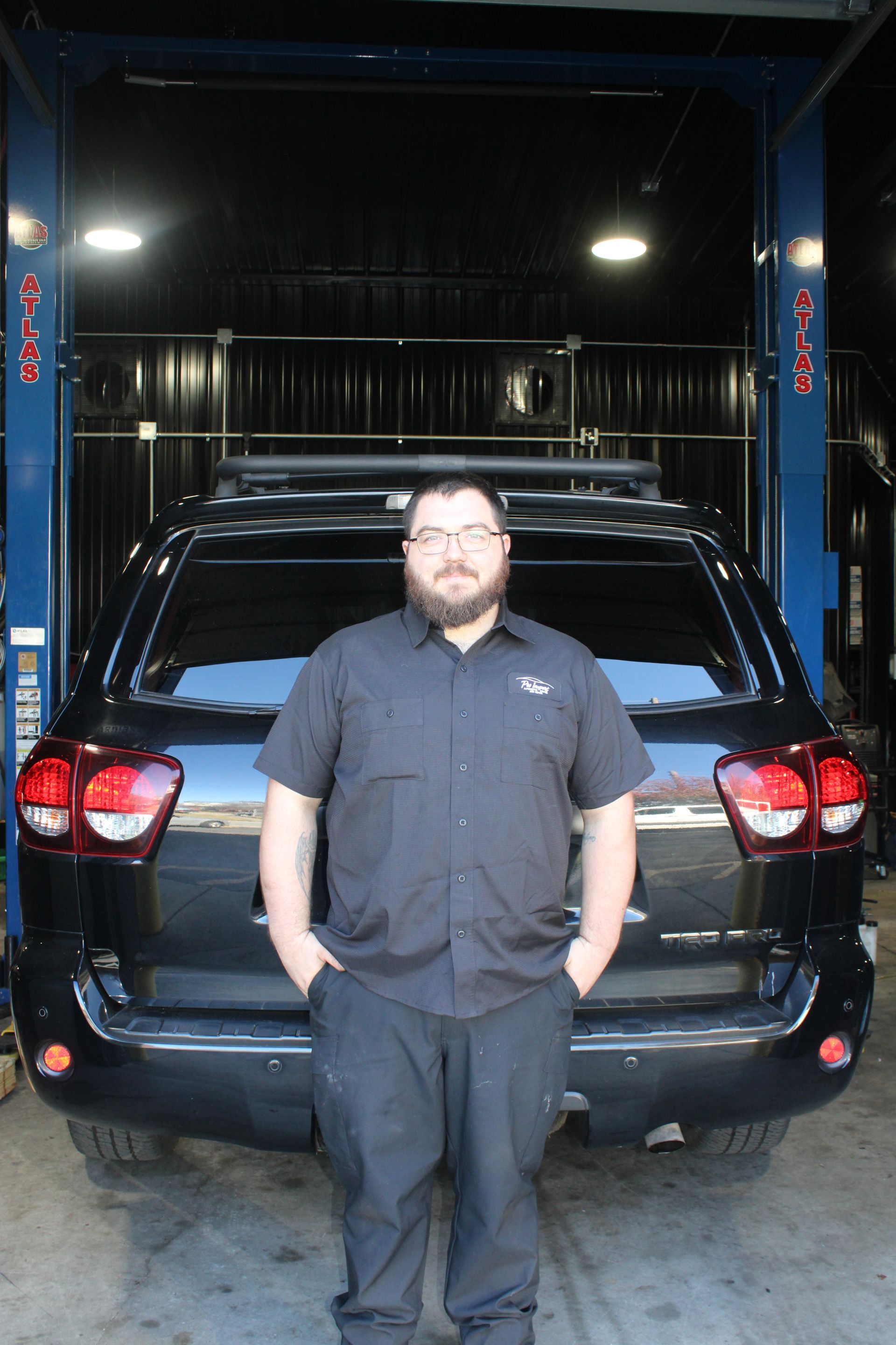 A bearded person with glasses wearing a black button-down shirt. | Pro Import Automotive Service and Repair