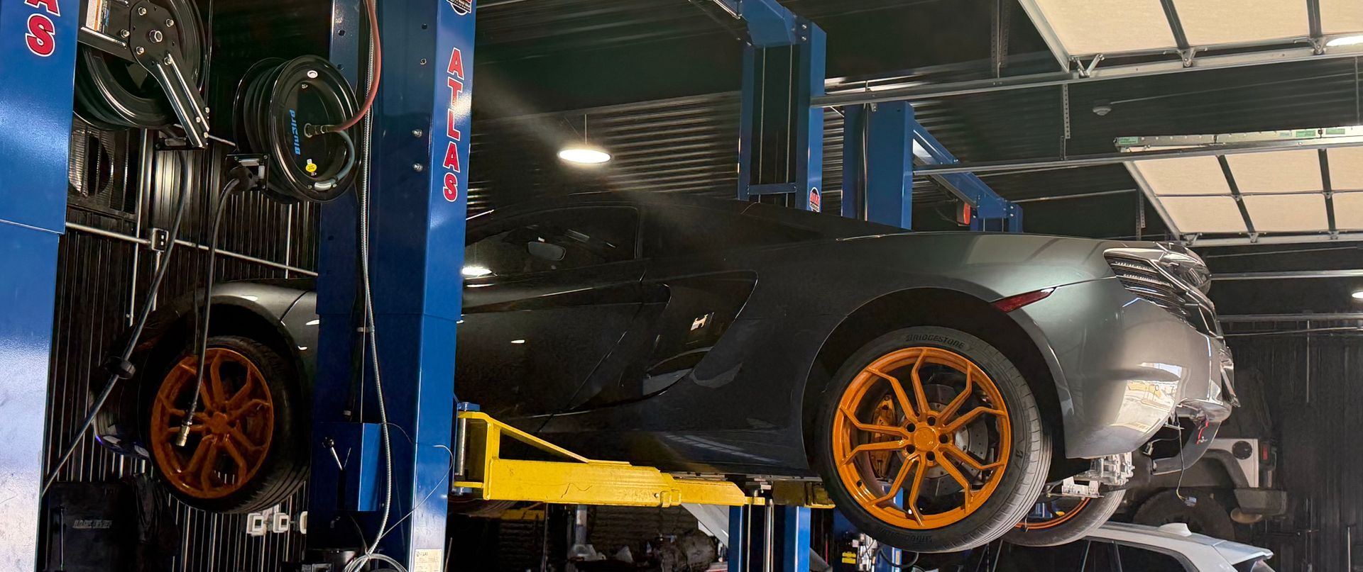 Gray sports car with orange rims on a lift inside an auto shop. | Pro Import Automotive Service and Repair