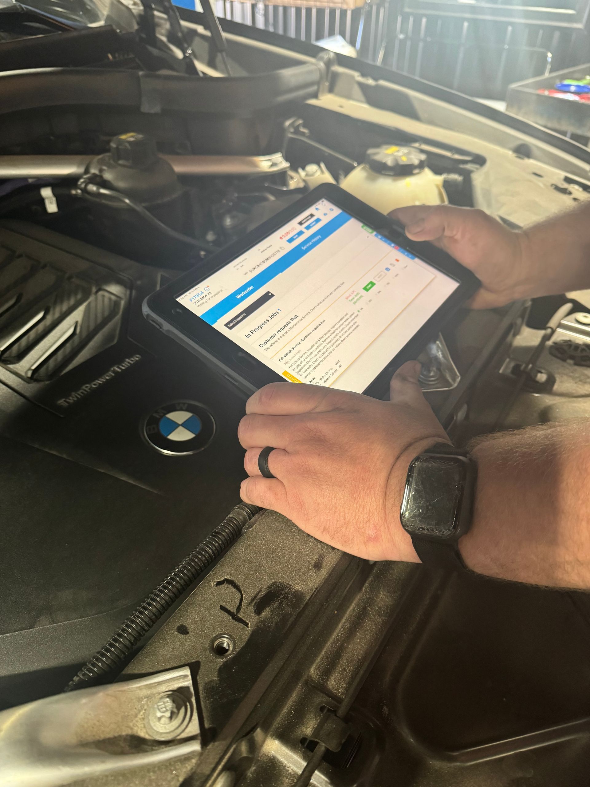 Hands using a tablet to inspect a BMW engine bay in a garage | Pro Import Automotive Service and Repair