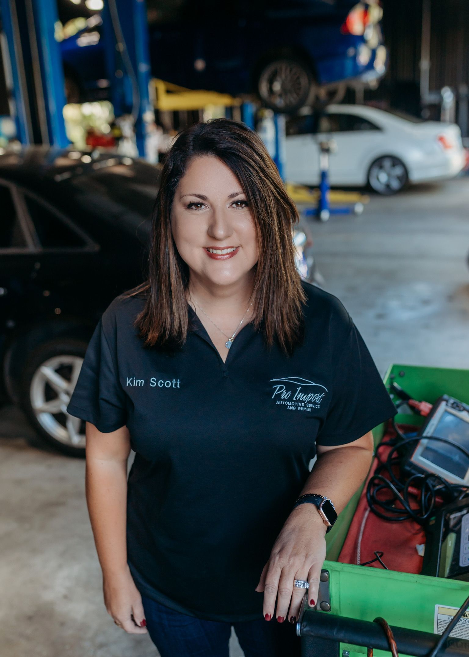 Woman in a black shirt standing in a garage beside a green cart and parked car. |Pro Import Automotive Service and Repair