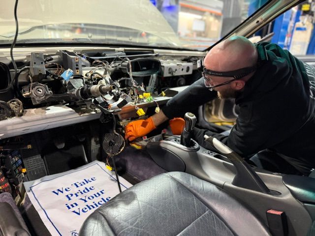 Mechanic using a power tool to work inside a stripped car interior and dashboard | Pro Import Automotive Service and Repair