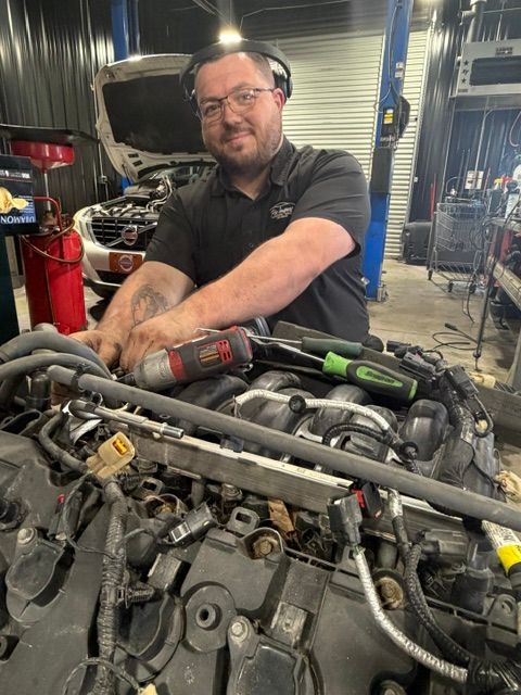 Mechanic smiling behind a car engine in a garage | Pro Import Automotive Service and Repair
