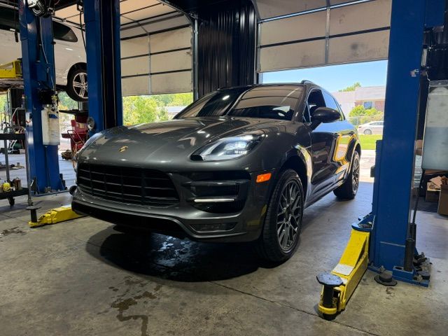 Black Porsche SUV in an auto shop between blue lifts, viewed from the front. | Pro Import Automotive Service and Repair