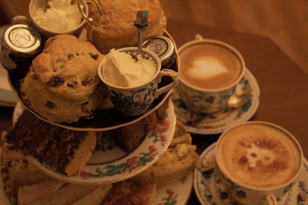 Three-tiered tray with scones, clotted cream, jam, and two cups of coffee with latte art.