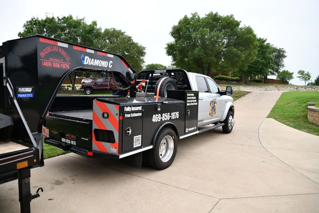 Black and silver drag racing truck on a trailer in a driveway, with trees and lawn nearby