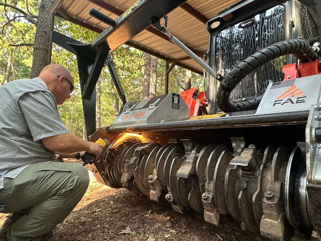 Mechanic grinding the track of a large machine under a shed, with sparks flying.