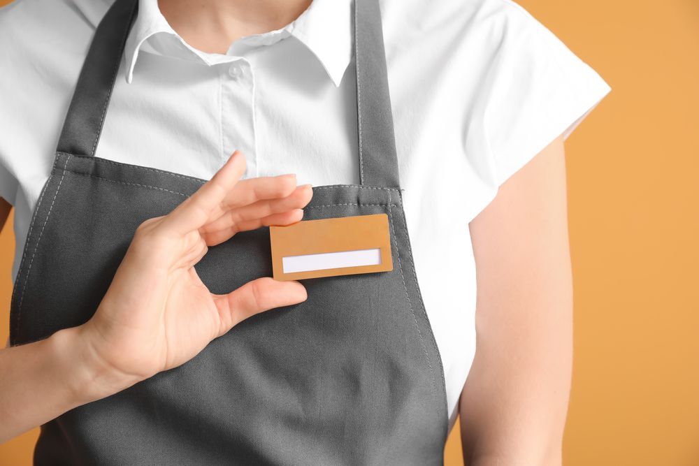 A Woman in An Apron Is Holding a Name Tag  — Jimani Trophies & Engraving in Dapto, NSW