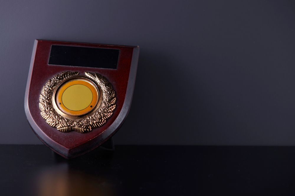 A Wooden Plaque with A Gold Circle in The Middle Is Sitting on A Table — Jimani Trophies & Engraving in Dapto, NSW