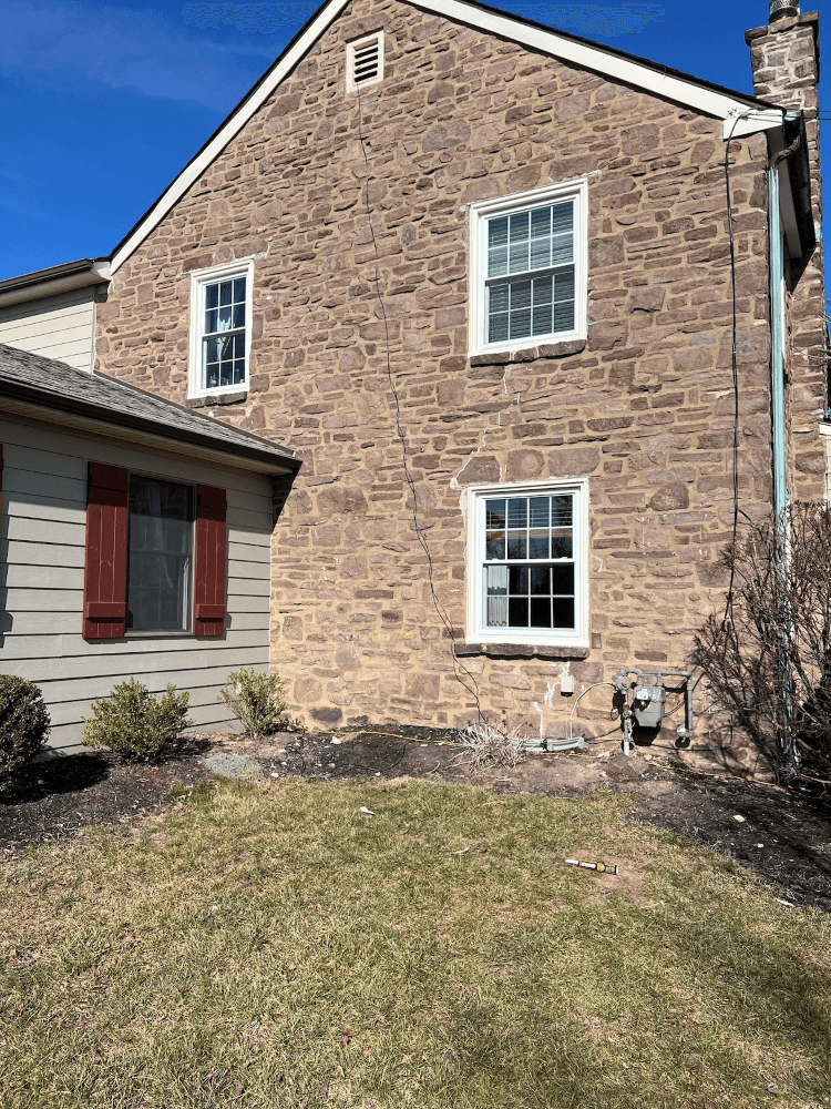 Stone house exterior with white-trimmed windows and a red-shuttered side wall above a grassy yard