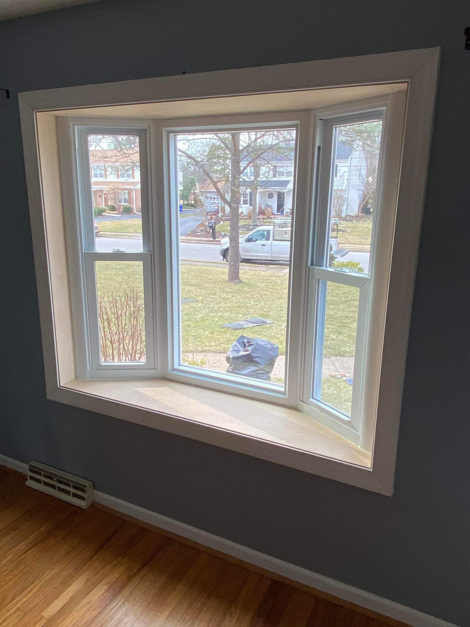 Bay window with white trim overlooking a suburban street, with sunlight and hardwood floor inside