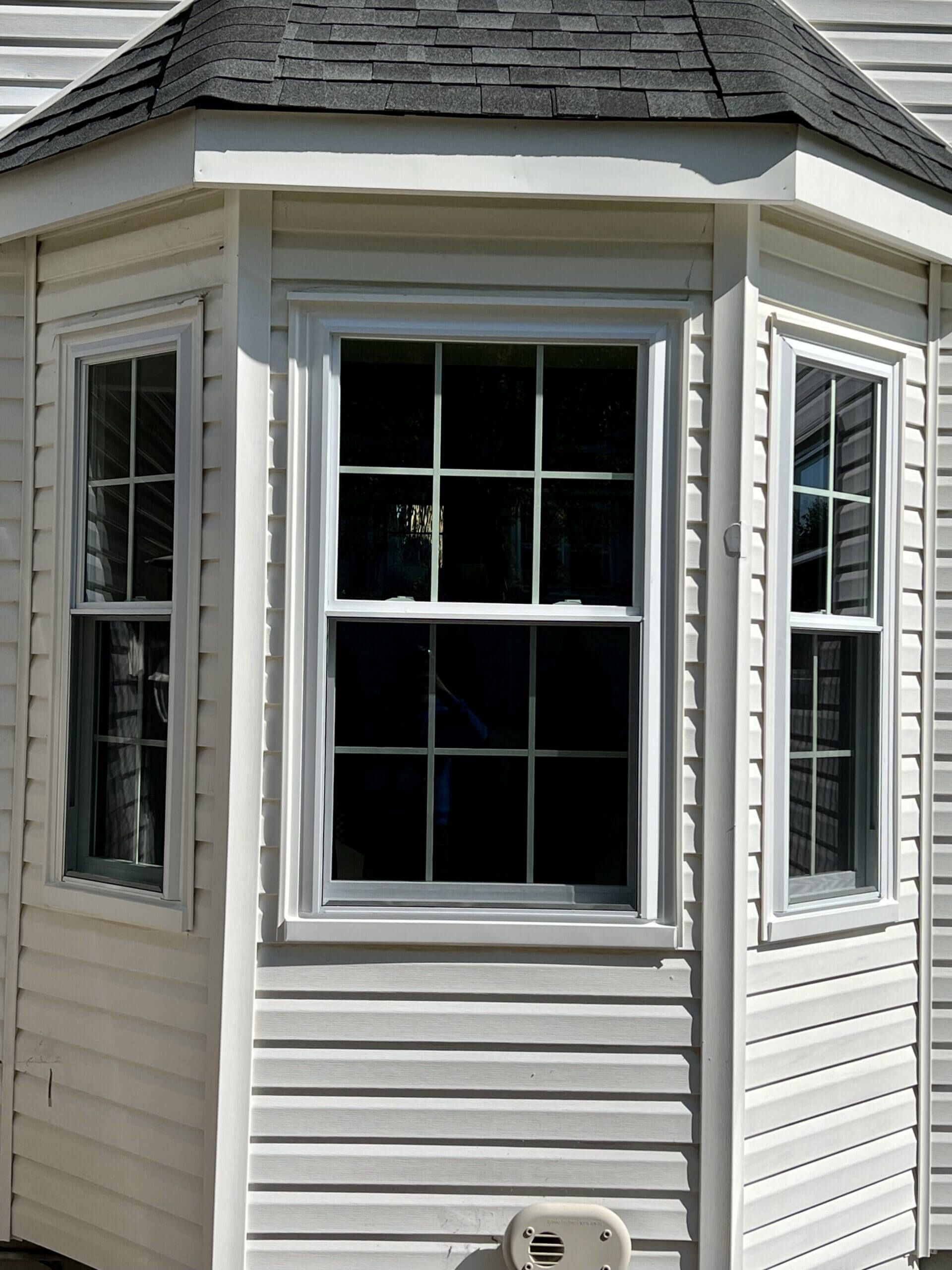 White bay window on a house with gray shingle roof and white vinyl siding.