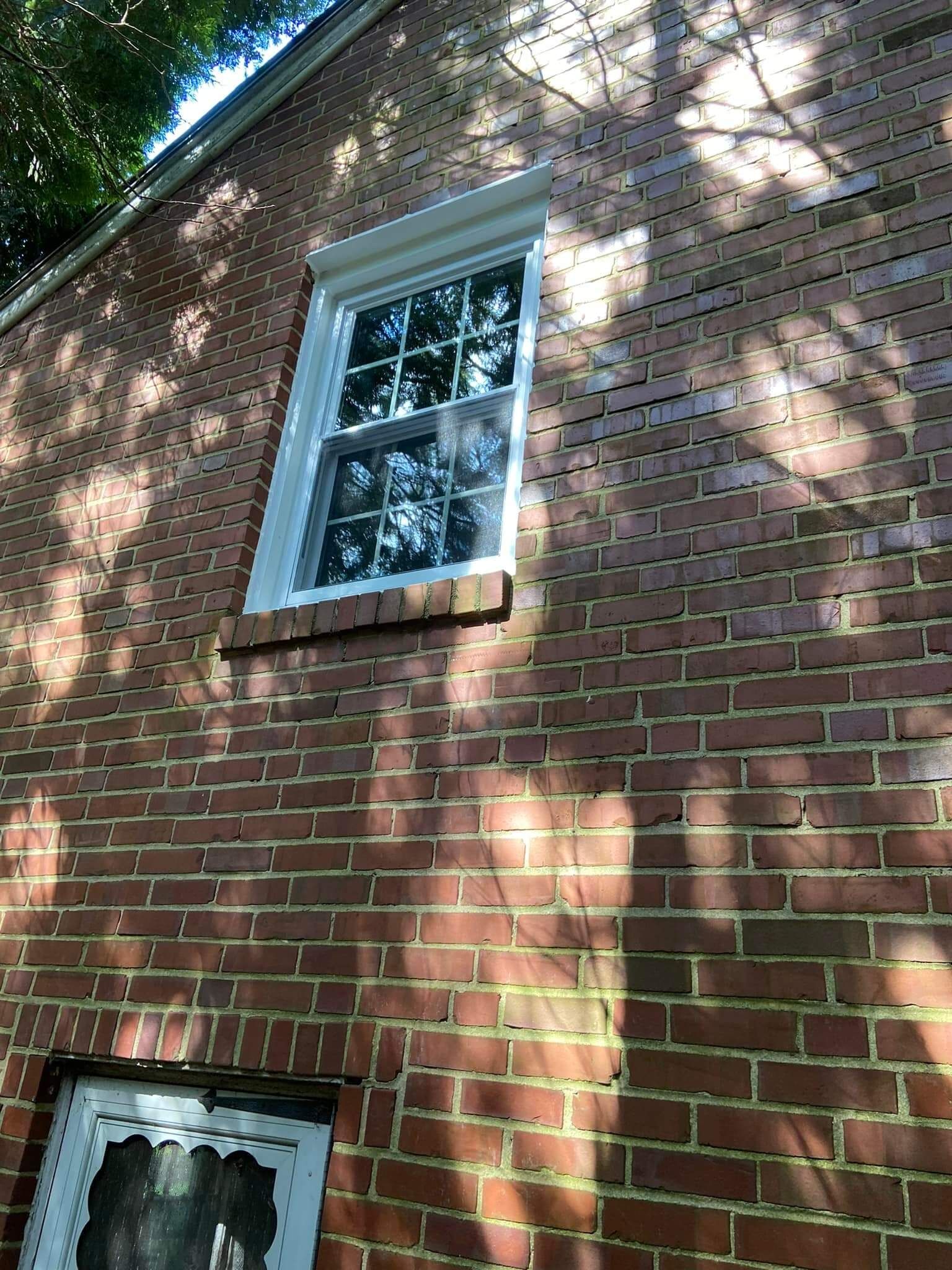 Red brick wall with two windows, one white-trimmed and one partially visible below.