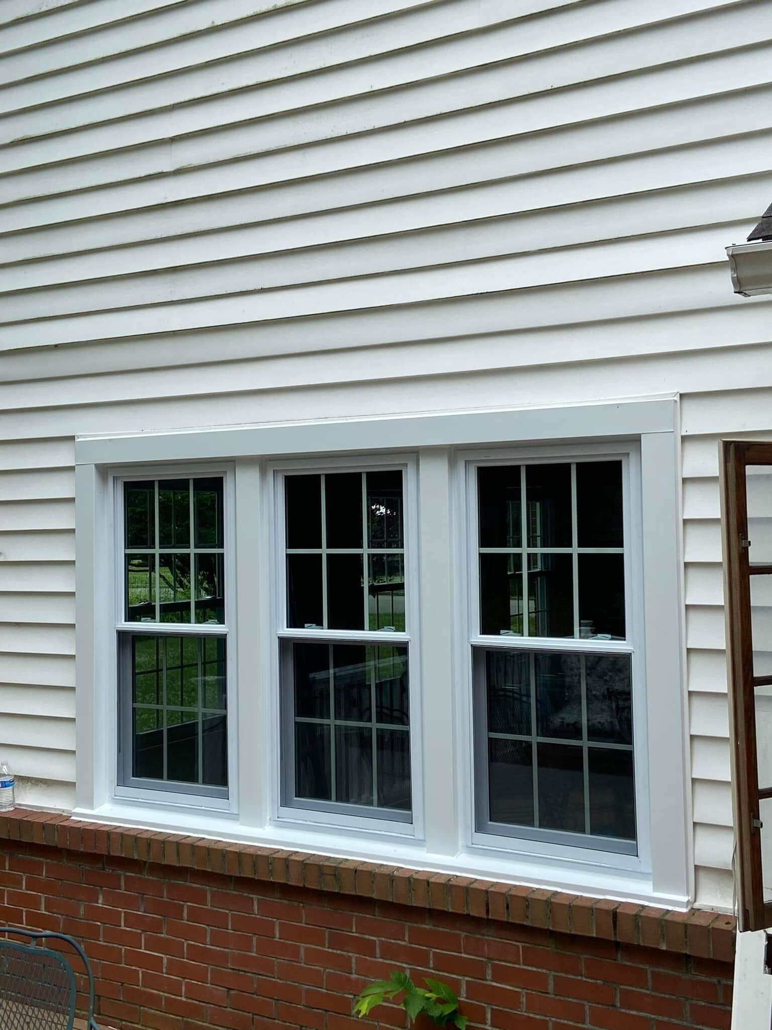 Three white-framed windows in a house exterior with white siding and a brick foundation.