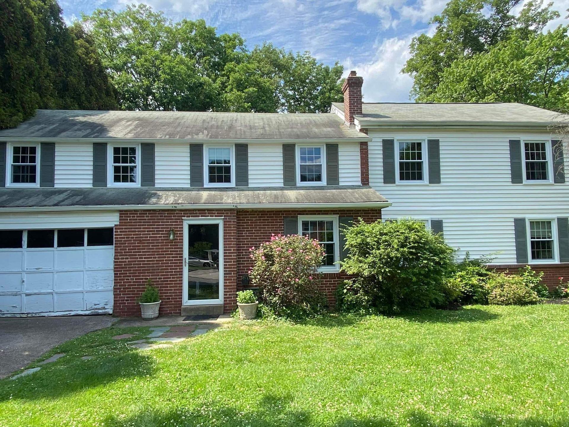 Two-story suburban house with white siding, brick entry, garage, and green lawn under a sunny sky