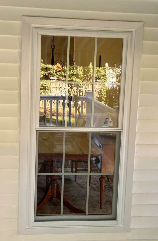 White-framed window on beige siding with a porch and chairs reflected in the glass
