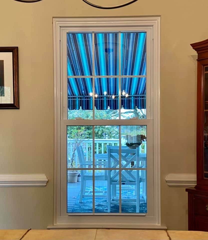 Window with white trim overlooking a blue-striped awning and patio railing outside.