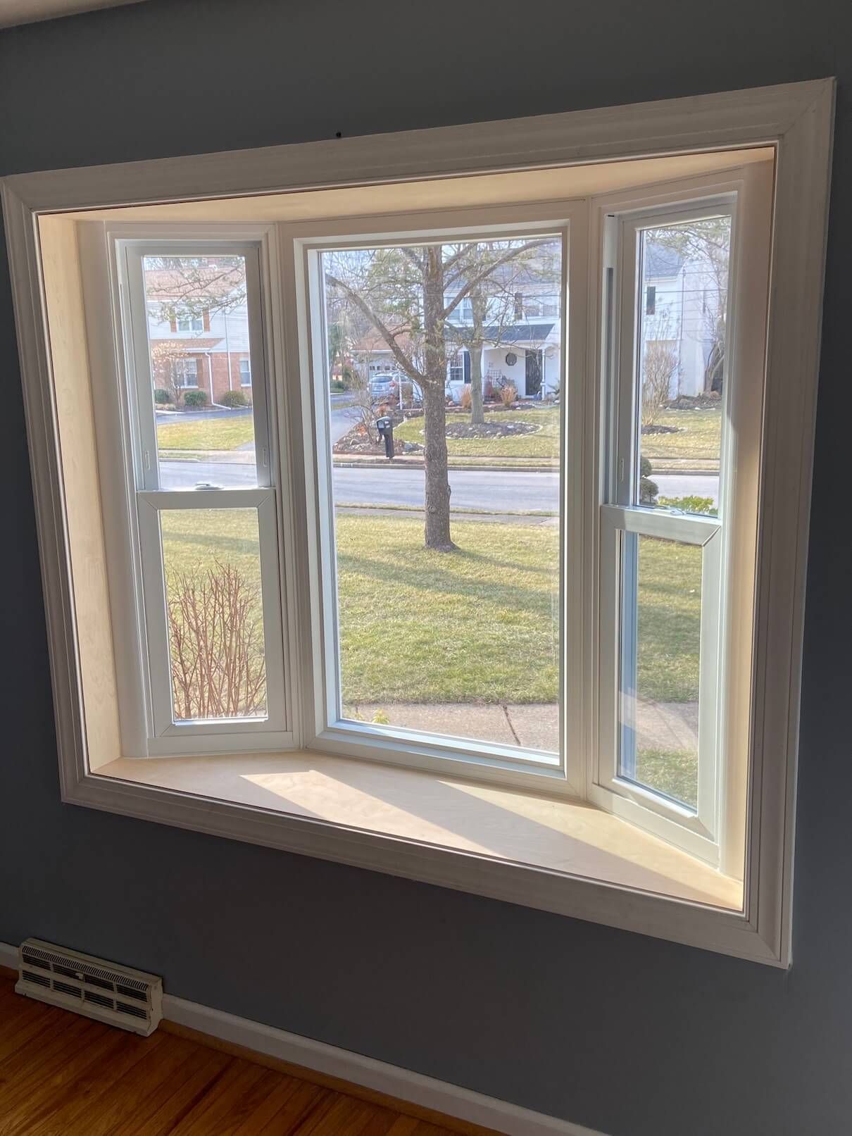 White bay window with three panes overlooking a grassy yard and street outside.
