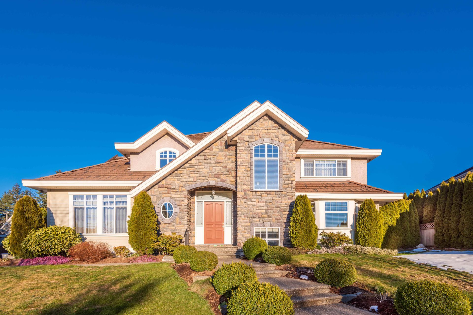 Large two-story brick suburban house with manicured landscaping under a clear blue sky