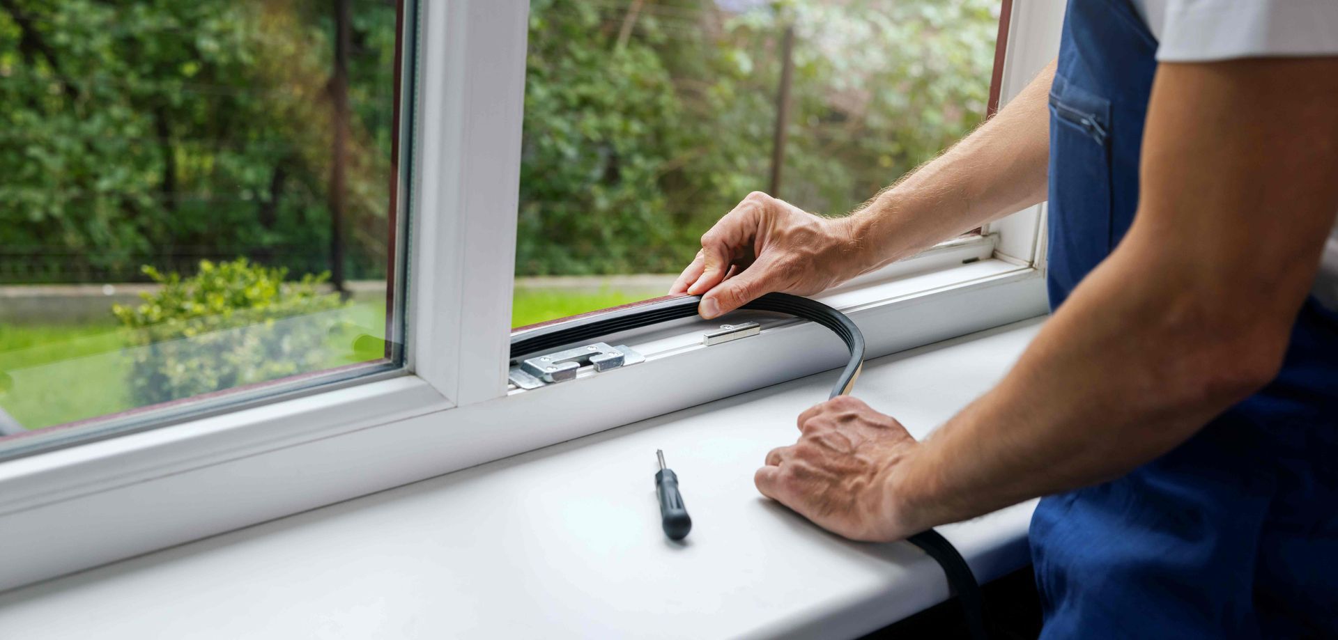 Hands adjusting a window lock on a white windowsill beside a green garden view