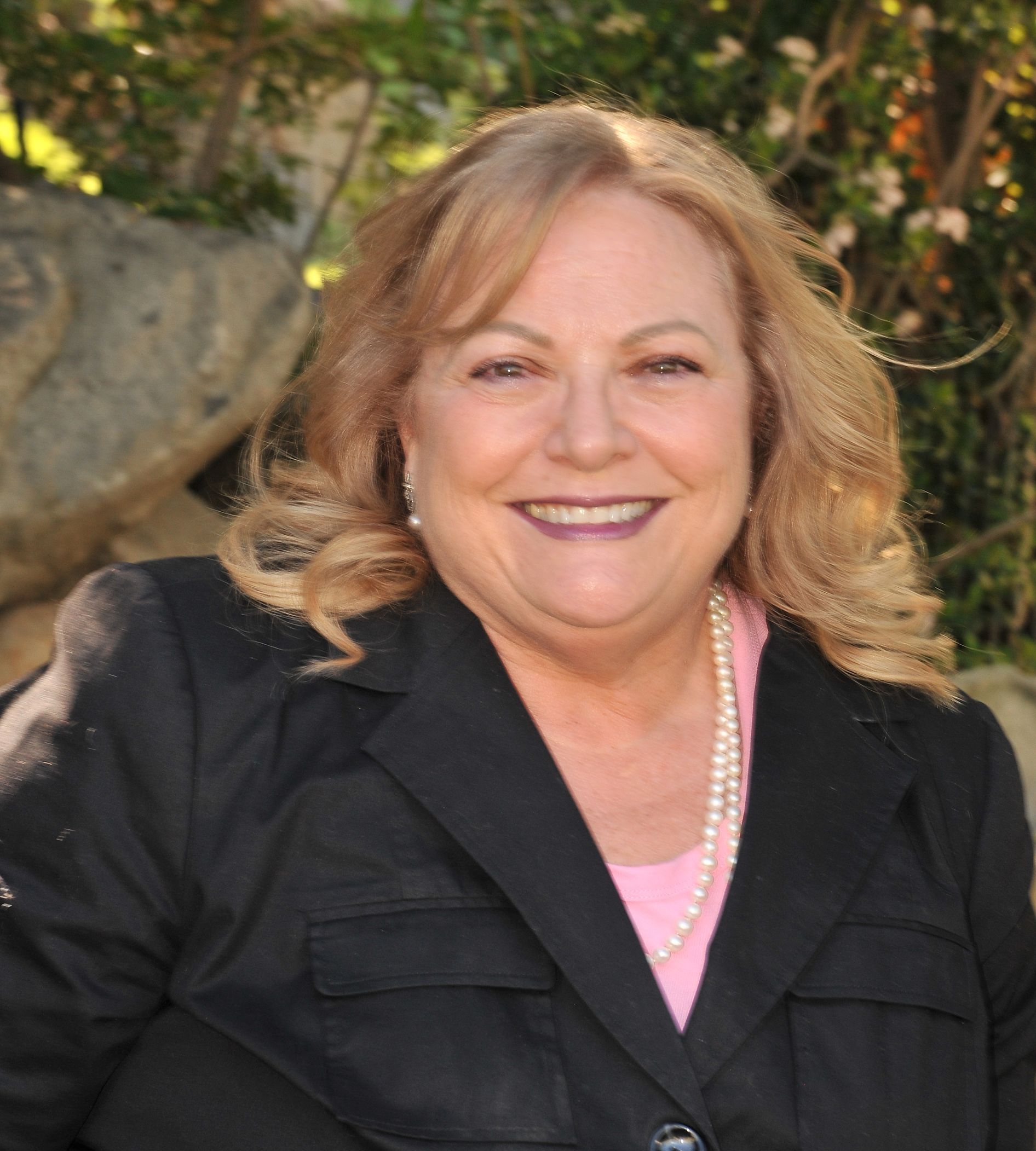 A woman wearing a black jacket and pearls smiles for the camera