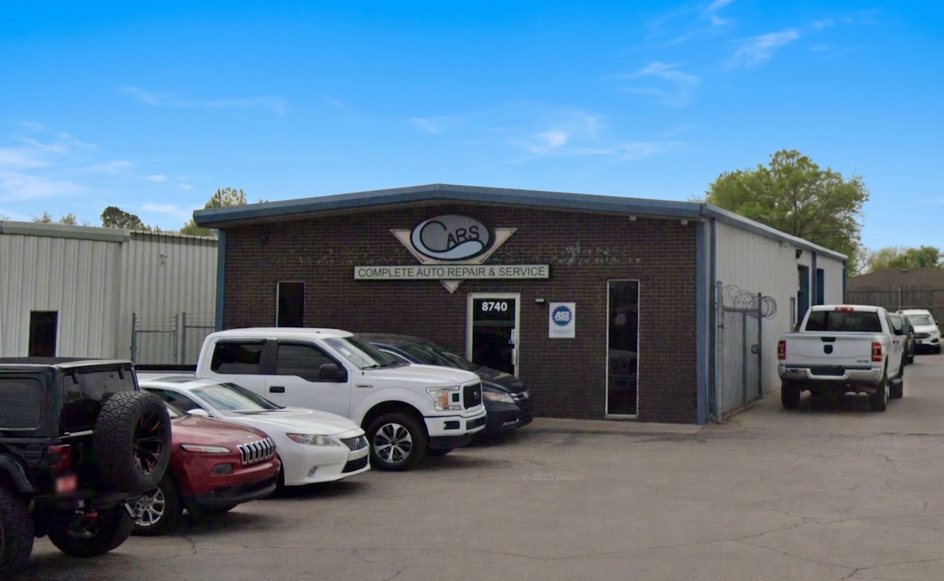 Auto repair shop exterior with parked cars and white truck under a clear blue sky