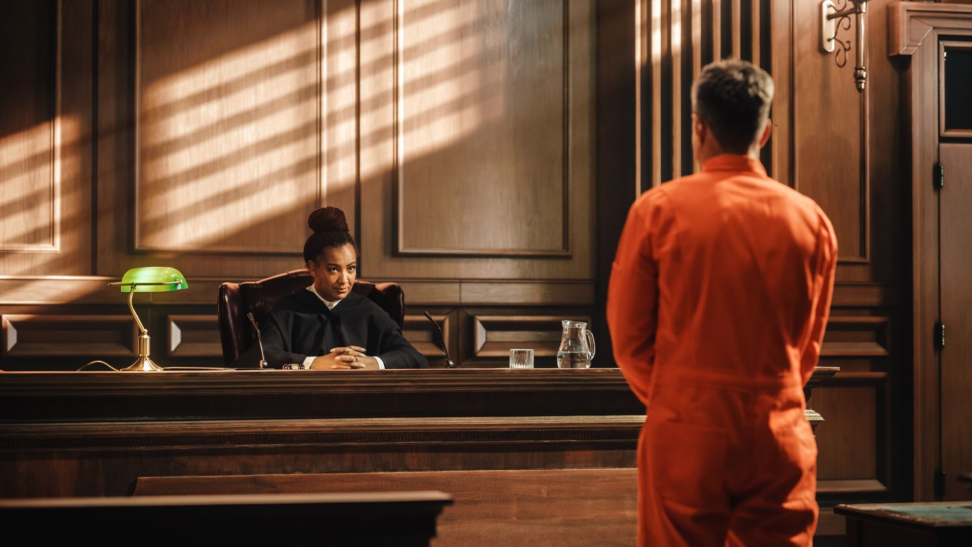 Judge in black robe watches man in orange jumpsuit in courtroom.