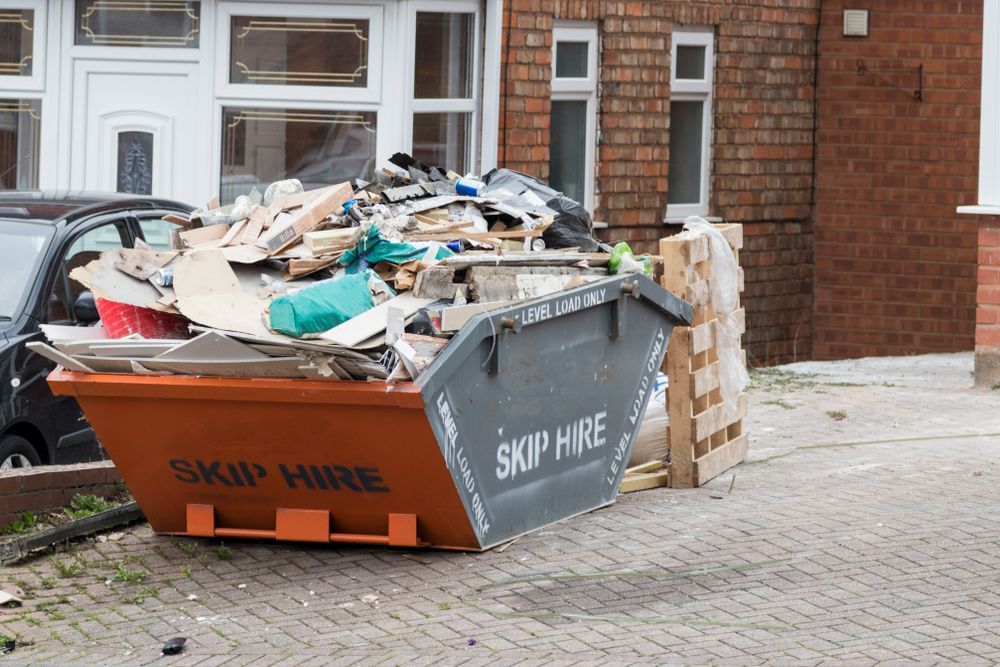 A Dumpster Filled With Garbage Is Parked In Front Of A Brick House — Liquid Waste Disposal in Port Macquarie, NSW