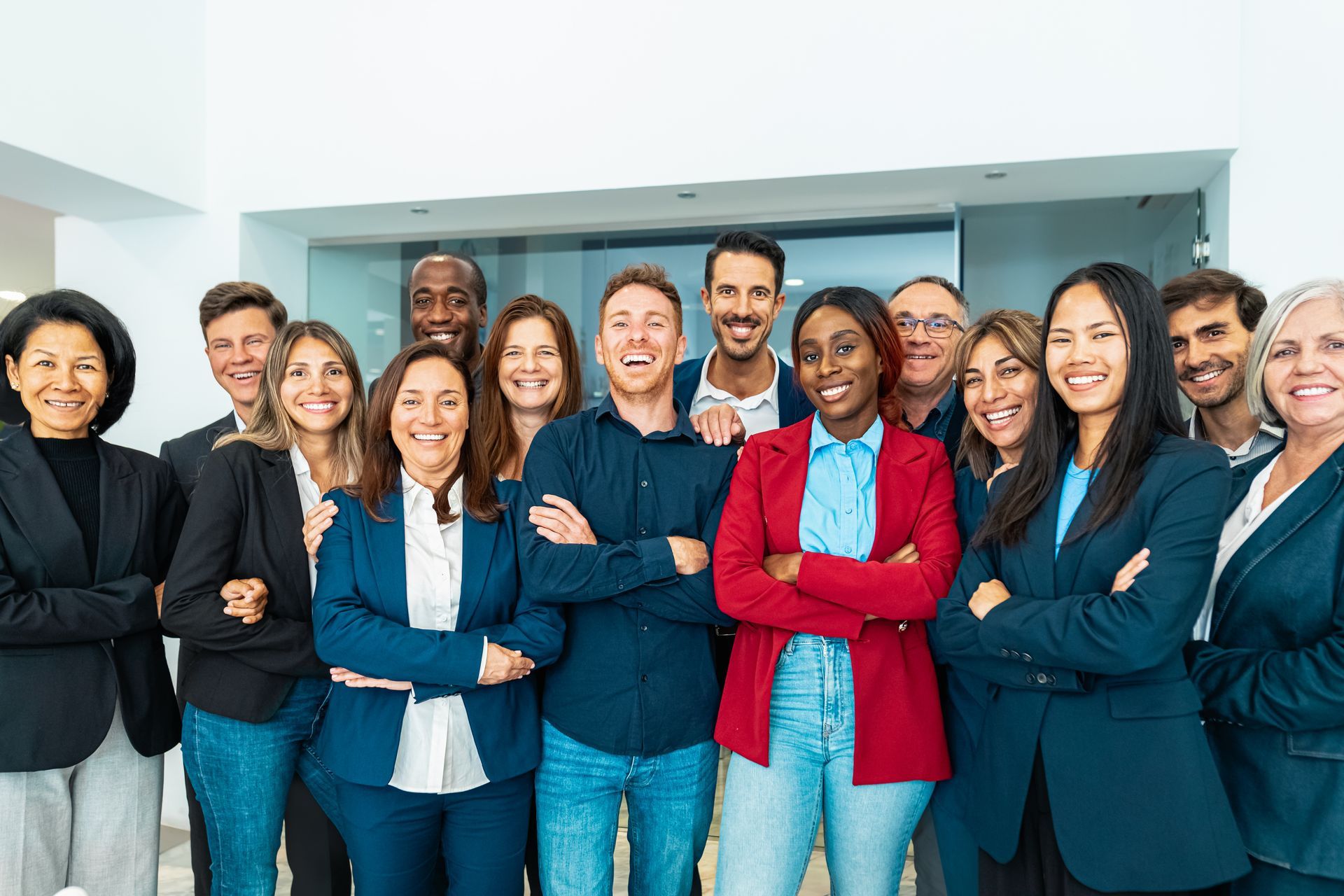 Group of diverse people in business attire standing close together with arms crossed, smiling.